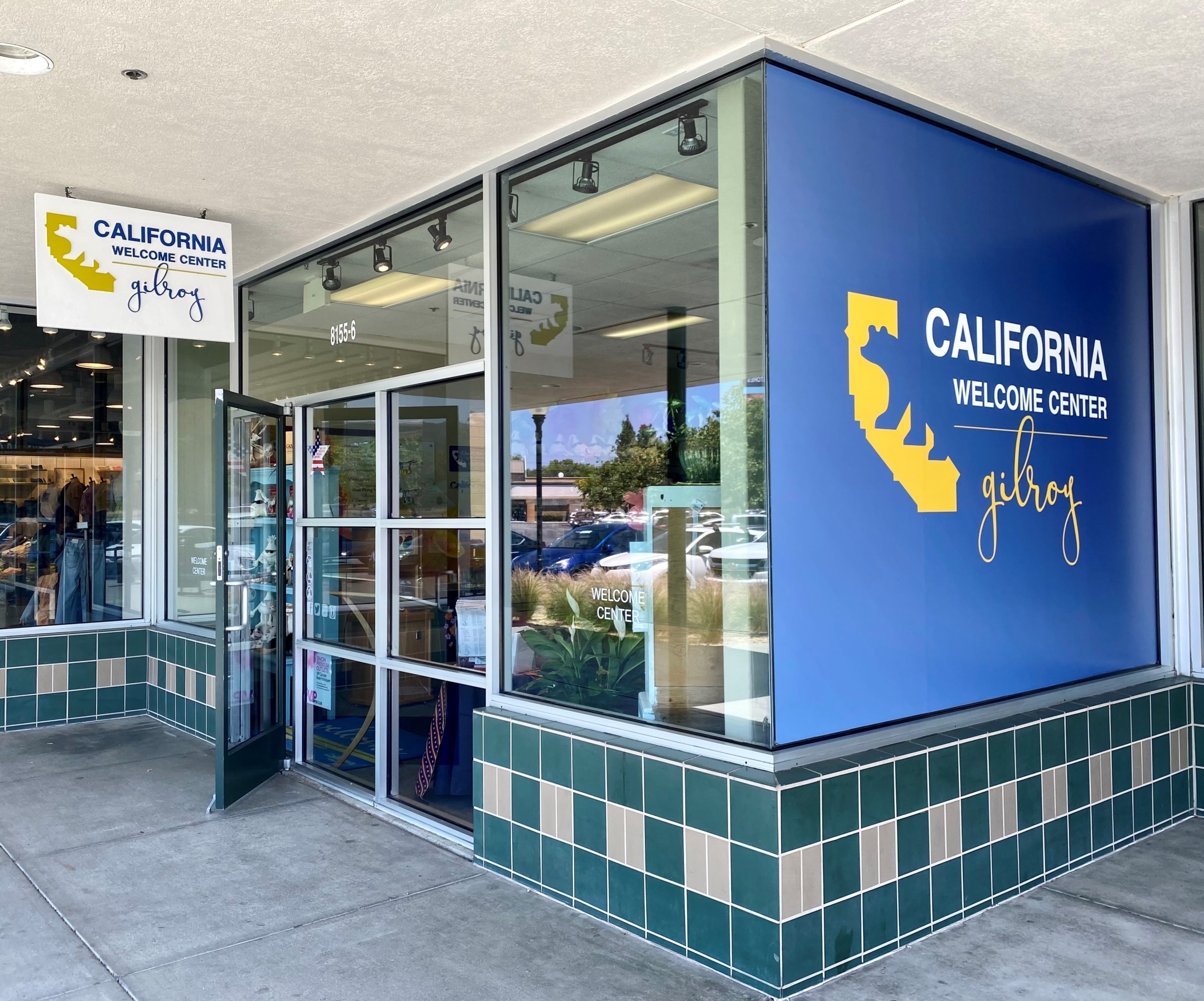 an exterior picture of the California Welcome Center with glass windows, green tiles along the bottom, and a blue vinyl cling on the right window