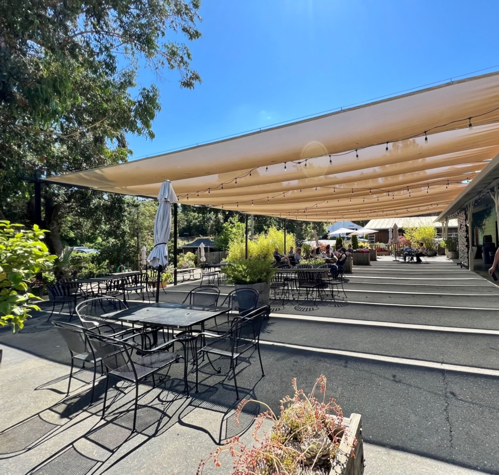 a patio with shade covering and people sitting at tables and chairs with wine