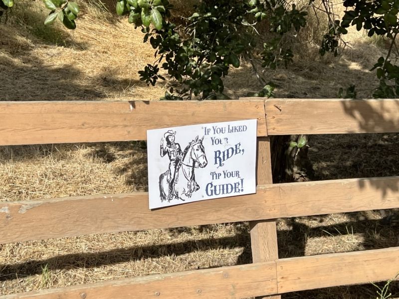a sign on a fence with a cowgirl picture says to tip your guide
