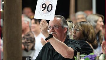 Man holding a paddle during an auction with the number 90 on it