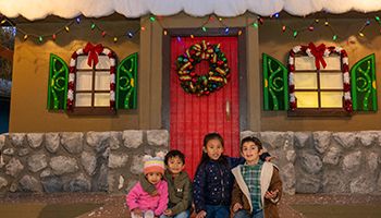 Two girls and two boys sitting smiling by a Christmas decorated house