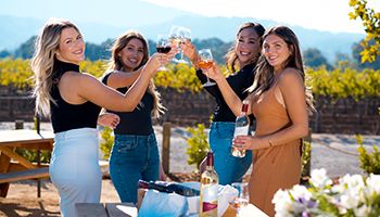 Four women cheering their wine glasses while smiling. Drinking red, white, and rosé wines.