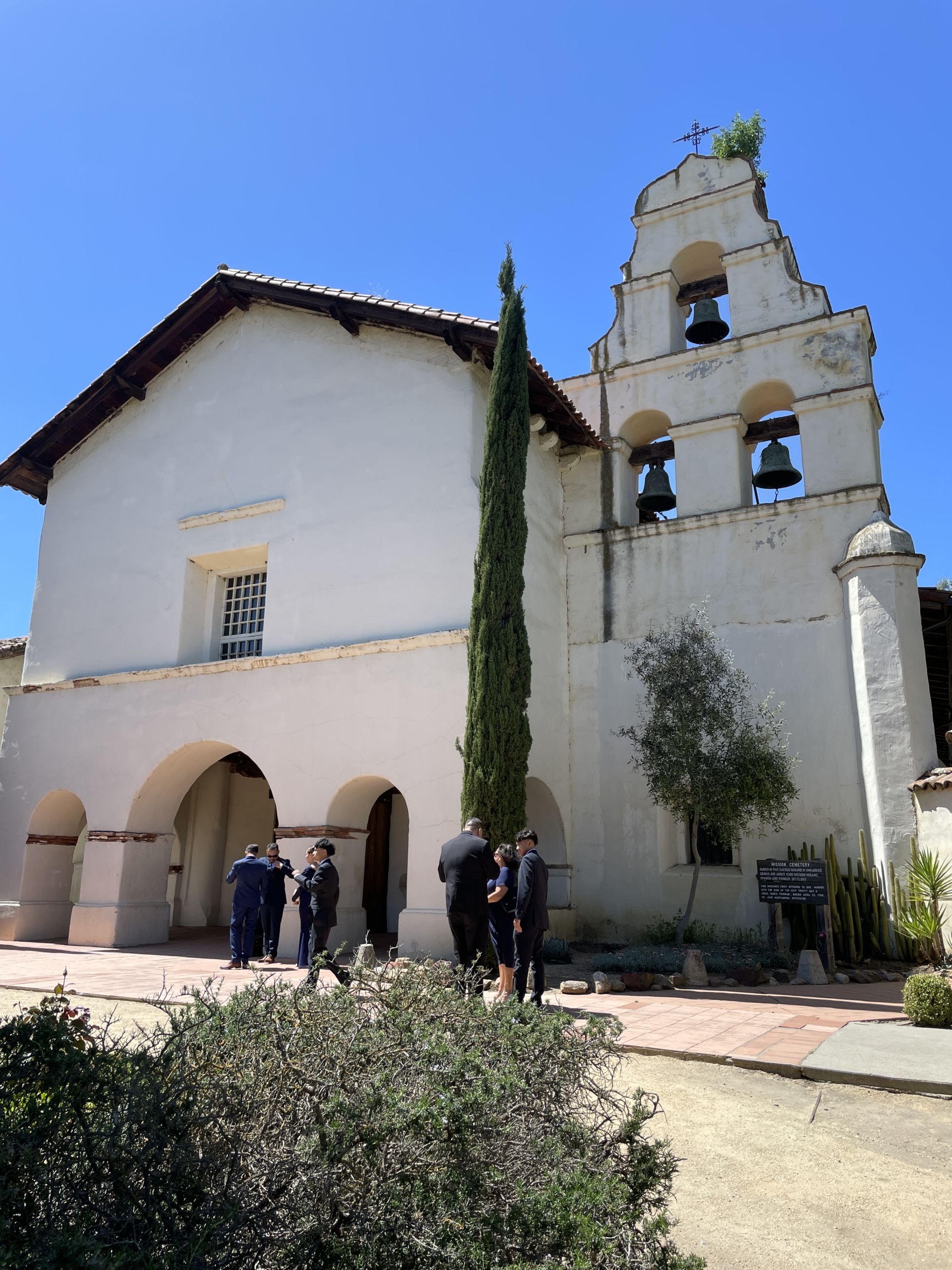 San Juan Bautista Mission. People stand in front of the Mission entryway and Bell Tower.