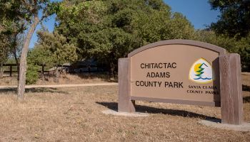 Chitactac Adams County Park sign with trees behind it, cropped photo